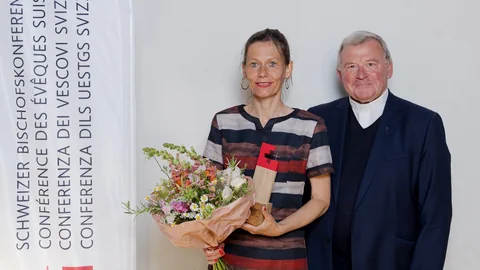 Frau mit Blumenstrauss neben Mann vor Banner der Schweizer Bischofskonferenz.